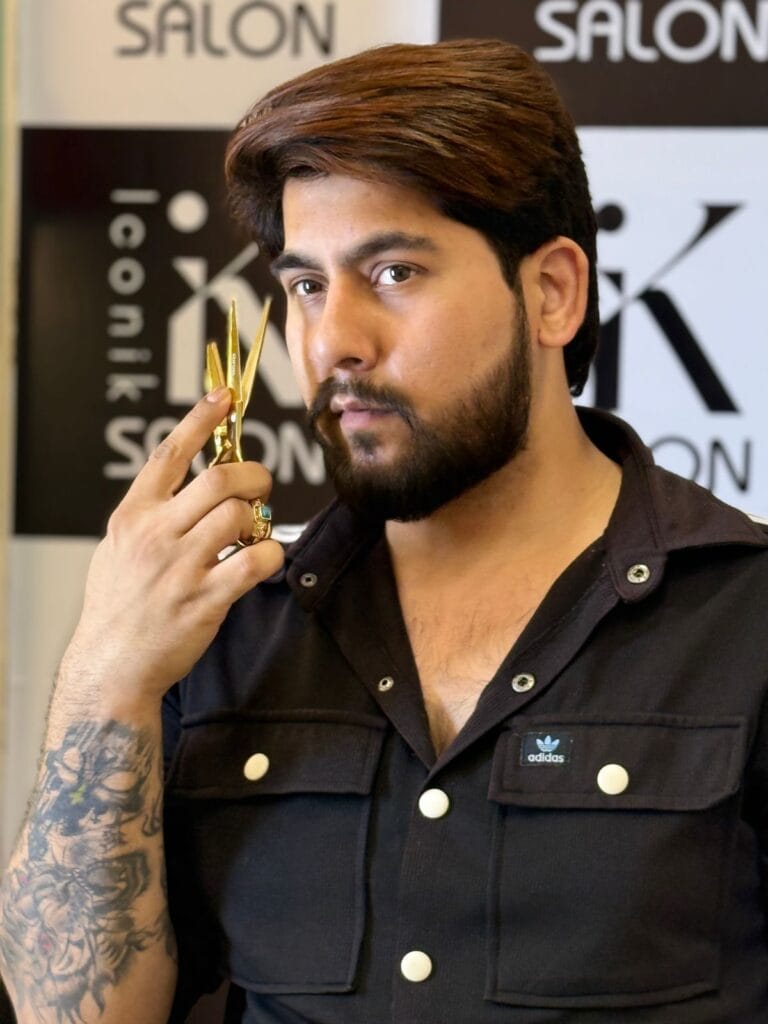 Image of salon's co-owner Kartik, holding golden scissors and on the background there is a banner on which the logo and name of iconik salon is mentioned